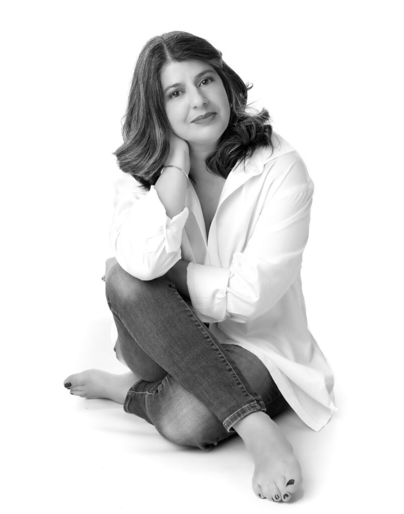 A woman sitting comfortably, smiling for a portrait taken by a glamour photographer.