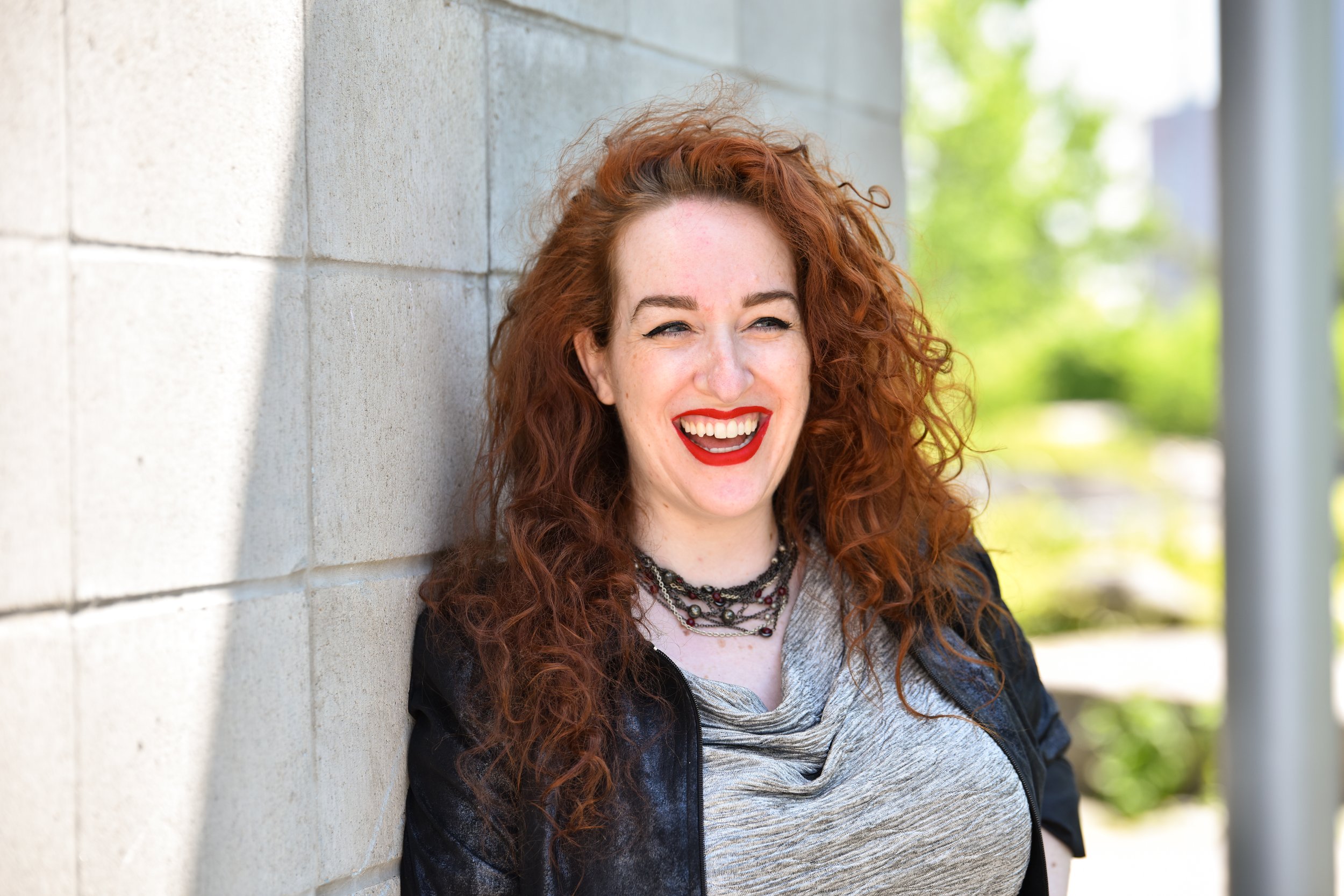 Red-haired woman laughing while leaning against a wall