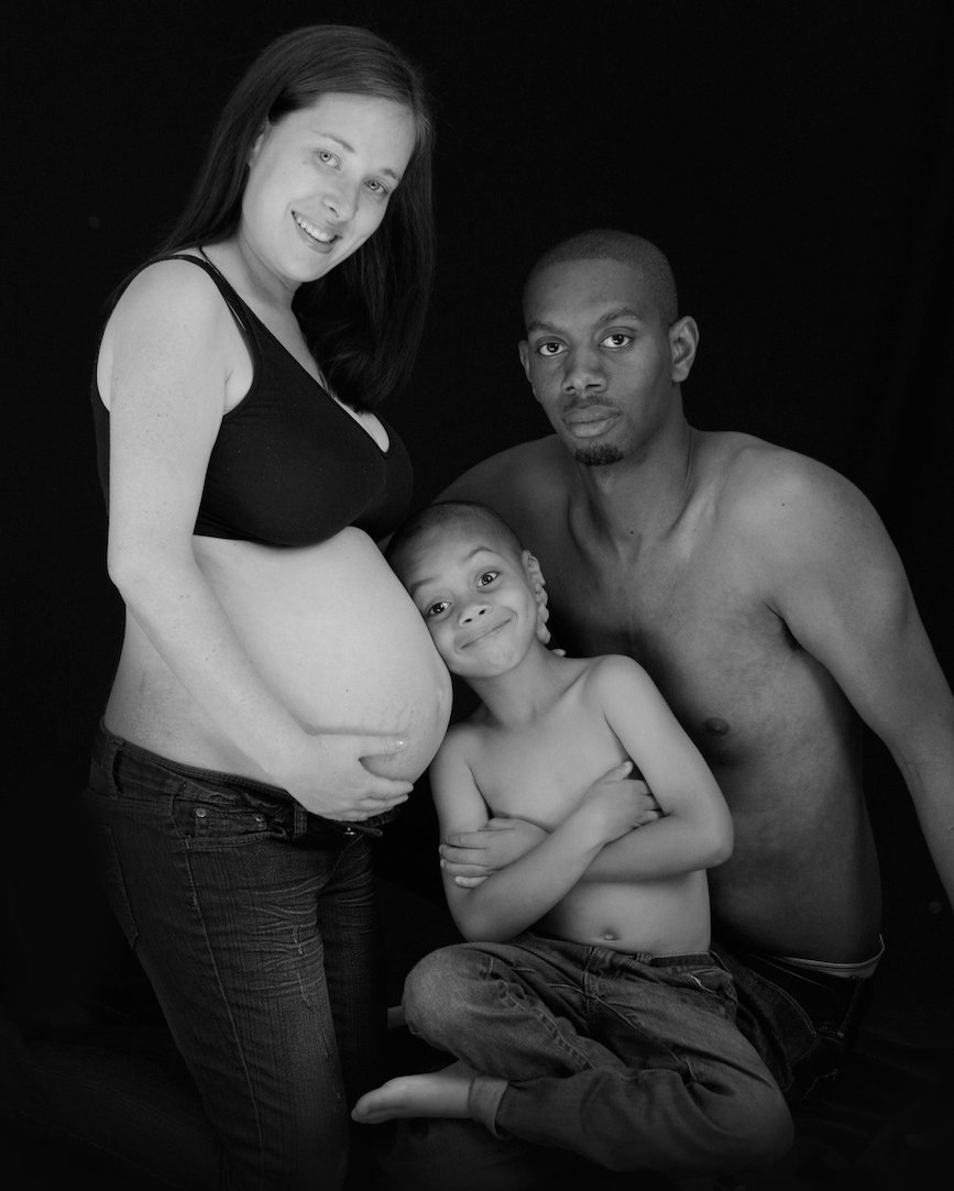 Pregnant woman with her partner and child, all smiling and embracing in a joyful family portrait. Toronto maternal photo shoots