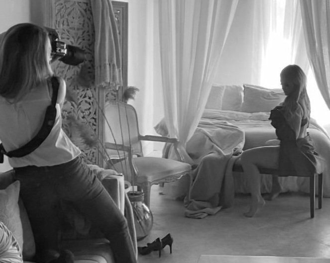 A glamour photographer taking photos of a woman posing on a chair in a beautifully decorated room.