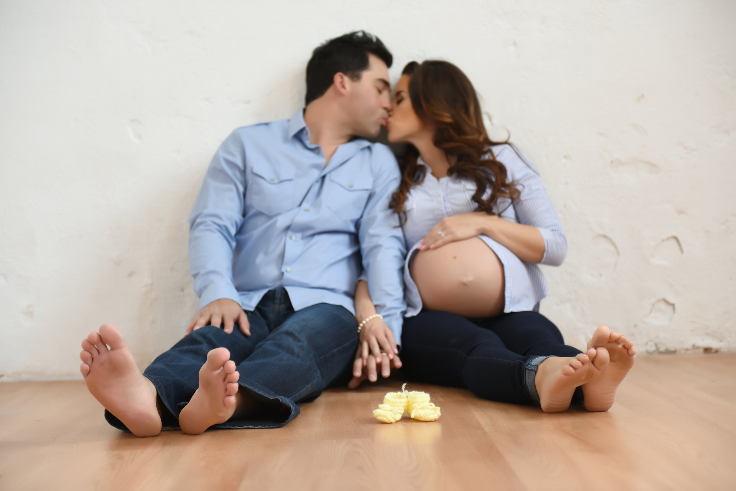 Expectant couple sitting on the floor, sharing a kiss with their hands gently placed on the woman's pregnant belly. Toronto pregnancy photography