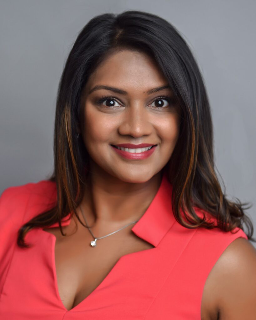 Professional corporate headshot of a woman with dark hair wearing a red top, smiling warmly.