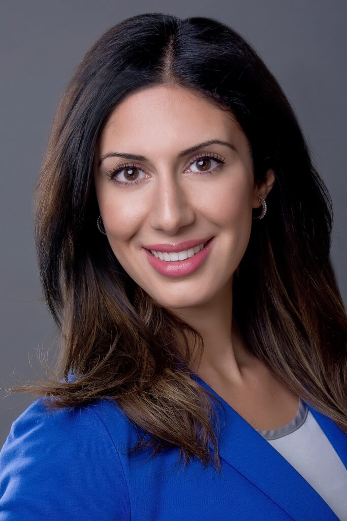 Professional corporate headshot of a brunette woman in a blue blazer, smiling brightly.