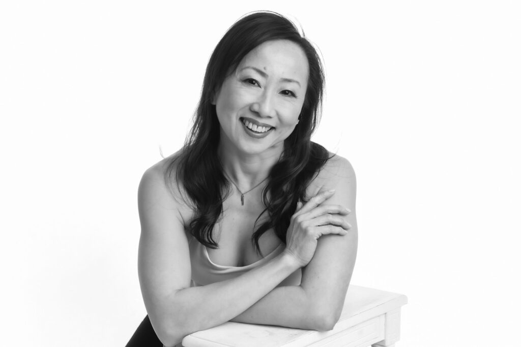 A woman smiling confidently, leaning on a white chair, captured by a glamour photographer