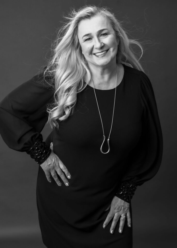 A confident woman smiling and posing in a black dress, captured by a glamour photographer.