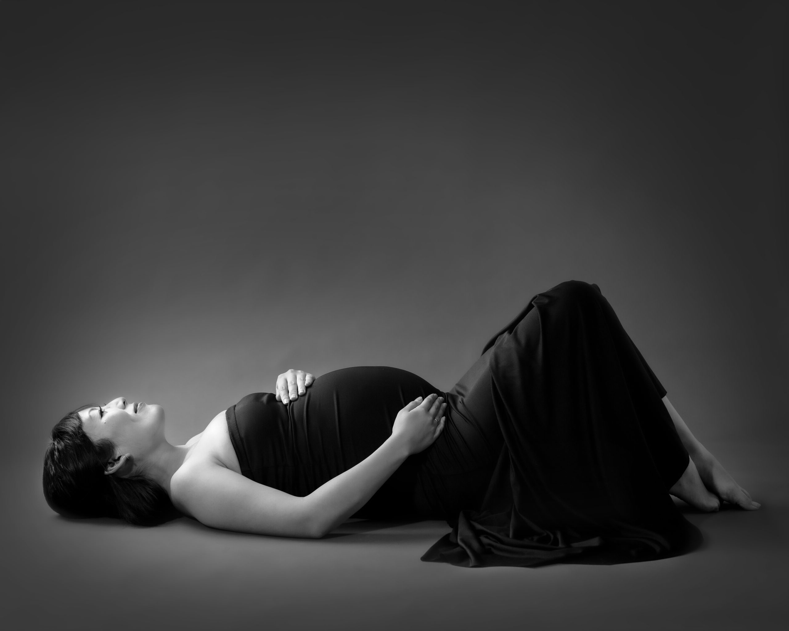 Pregnant woman portrait laying on a black backdrop