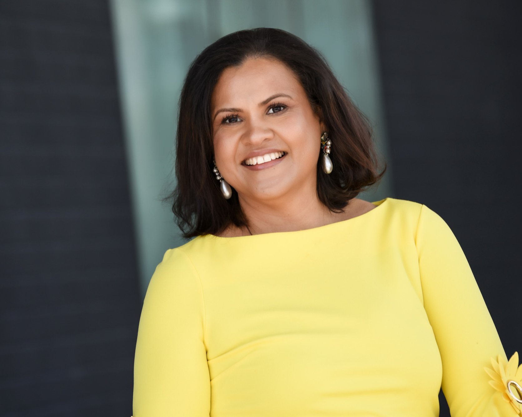 Woman in a bright yellow dress smiling warmly in an outdoor urban setting. corporate photographers