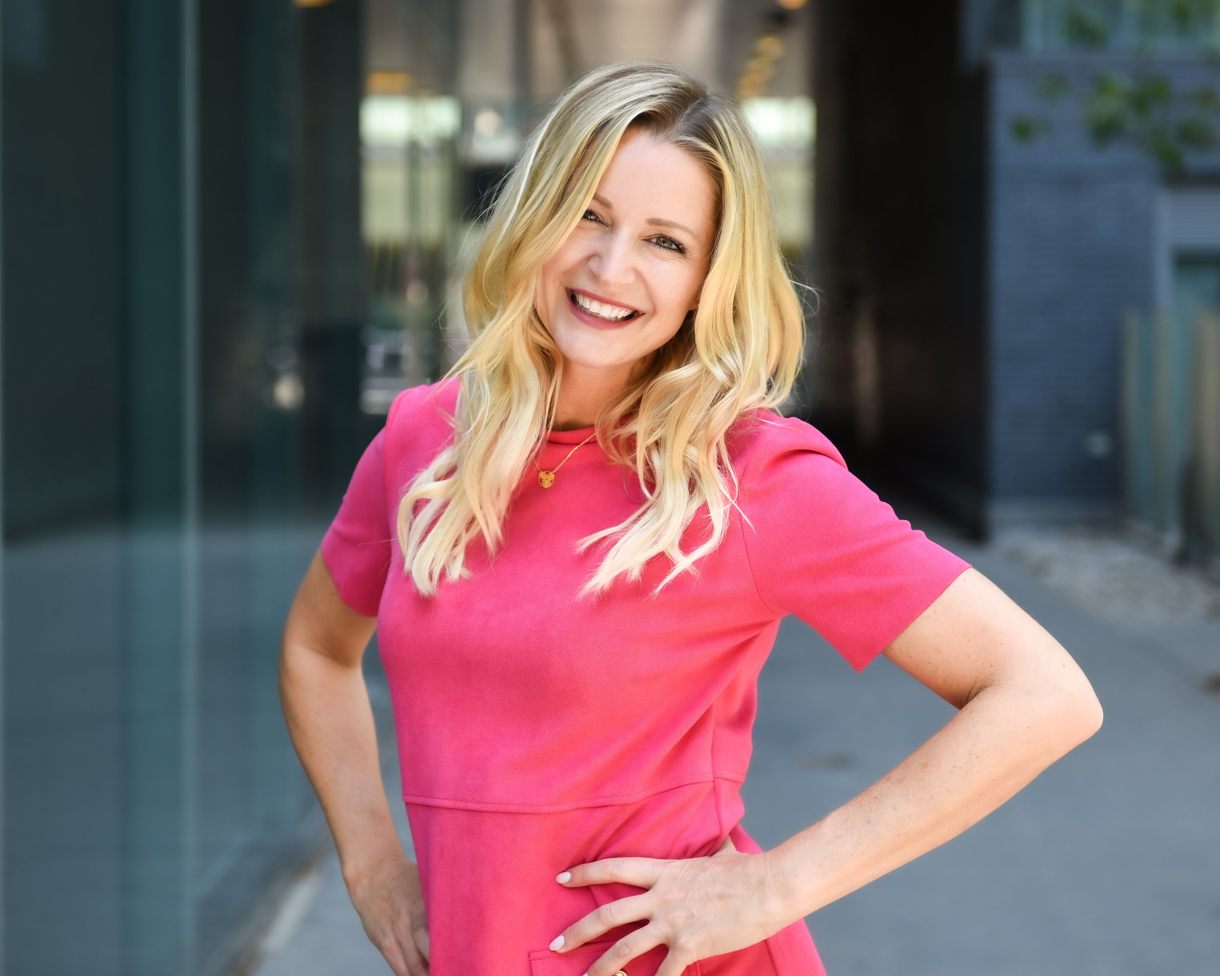 Happy woman in a bright pink dress posing confidently in an urban environment.