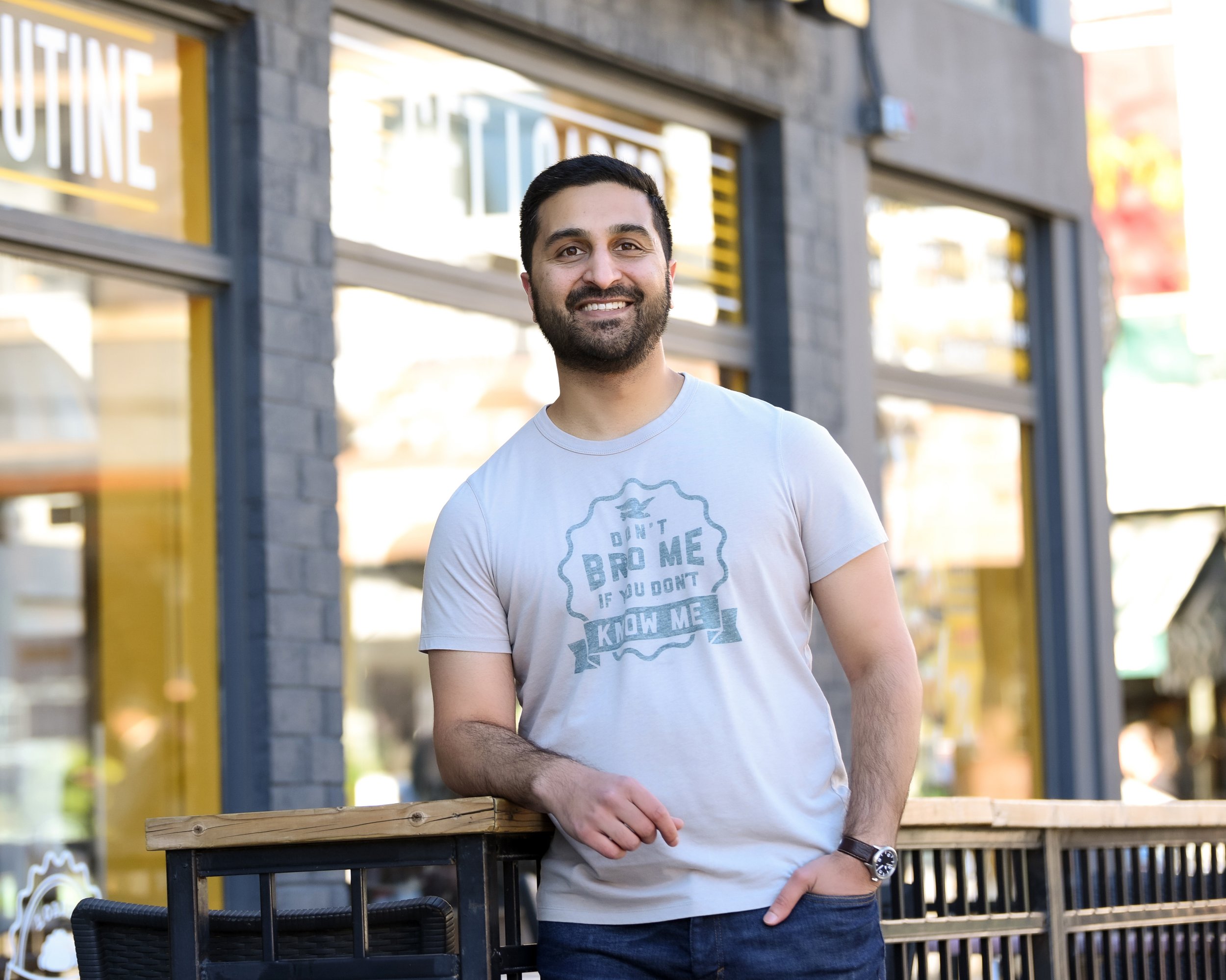 Man leaning against a railing outside a trendy restaurant with a welcoming smile.