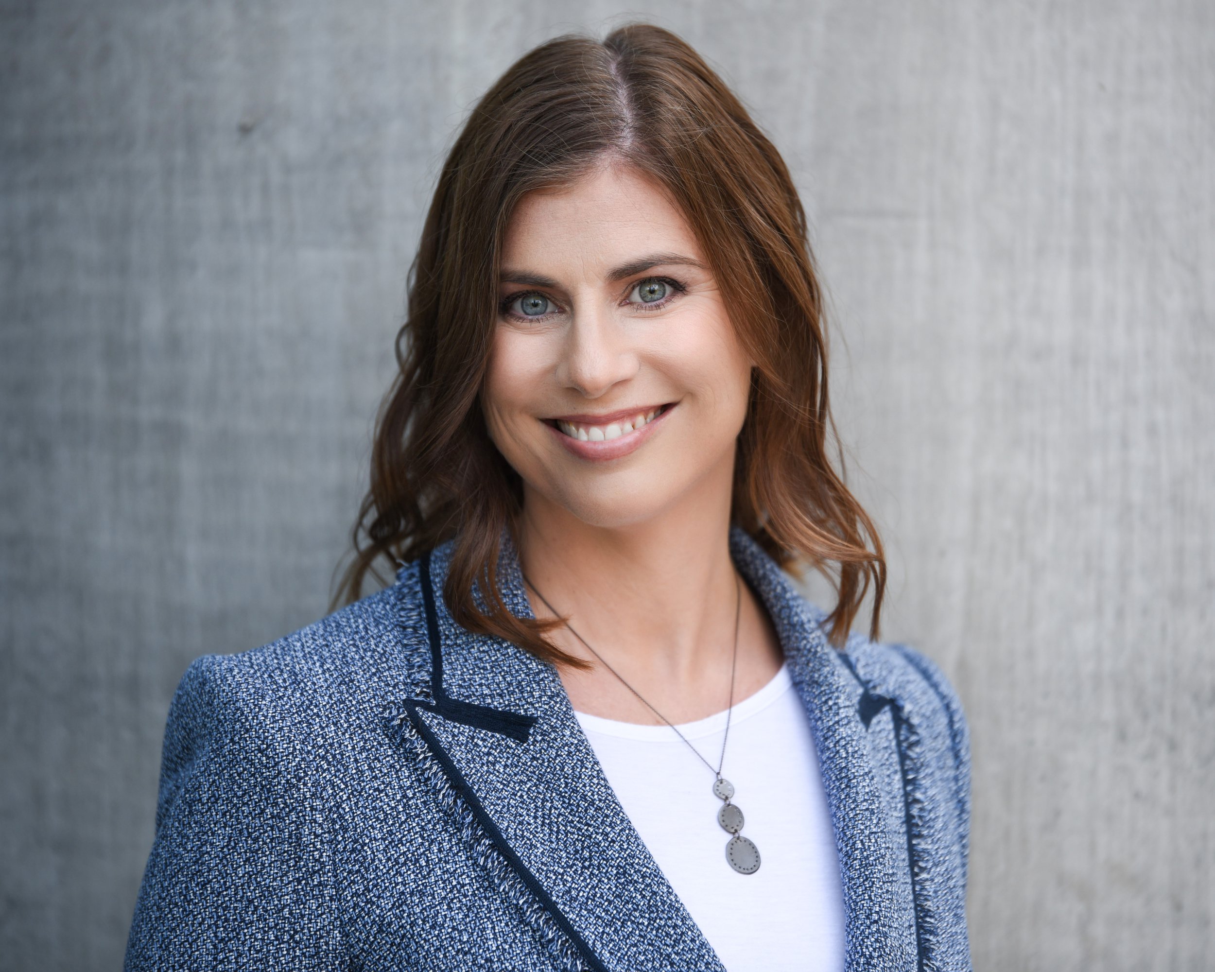 corporate photographers capture Smiling businesswoman in a blue blazer against a neutral background.