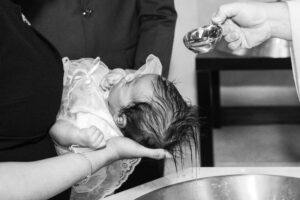 A priest pouring water over a baby's head during the baptism ritual, with the baby held over a font.