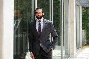 Young man's professional headshot outdoors by an office building glass wall.