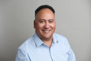 Smiling male counselor in a light blue shirt with a neutral background.