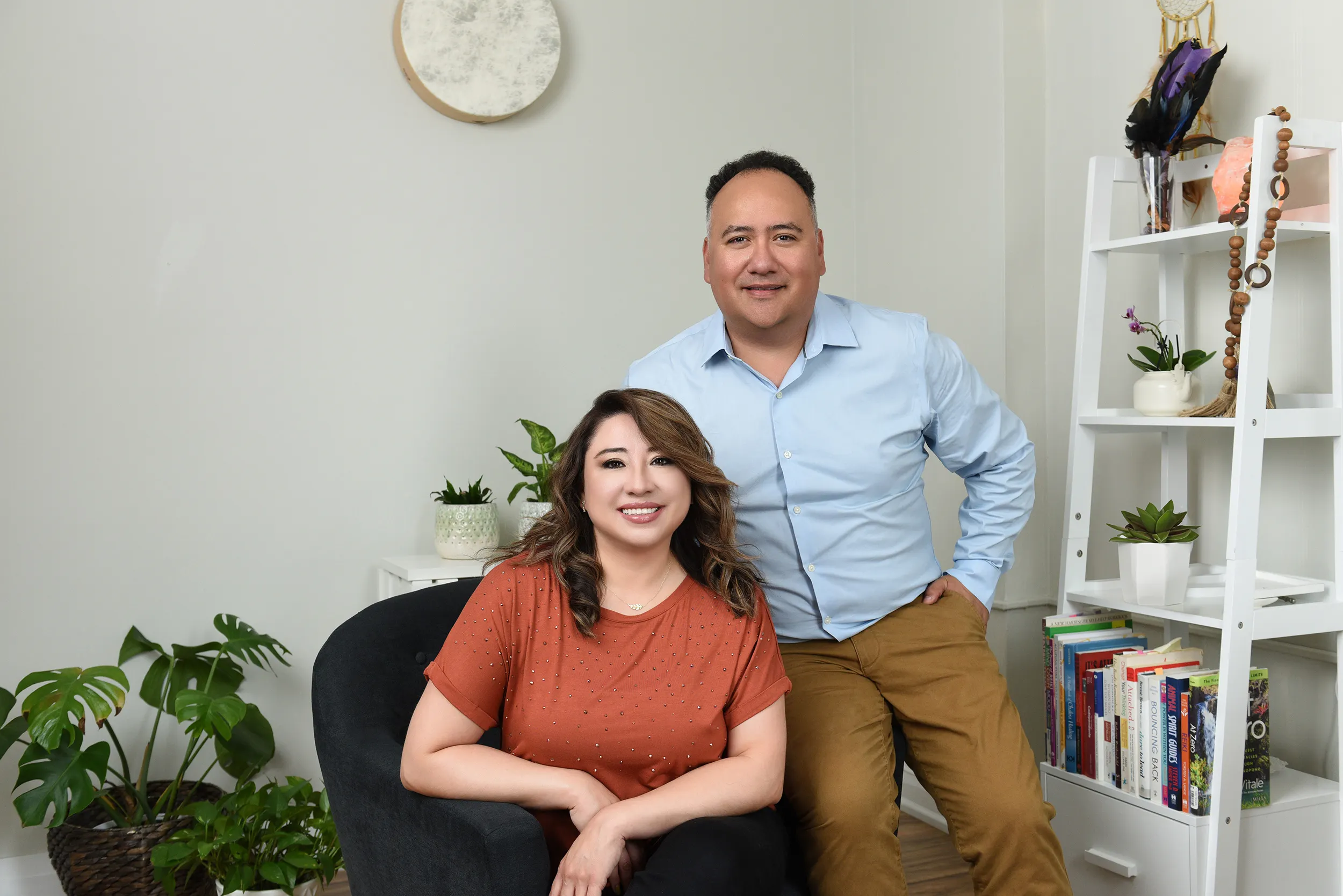 Two professional counselors posing together in a modern, plant-filled office setting.