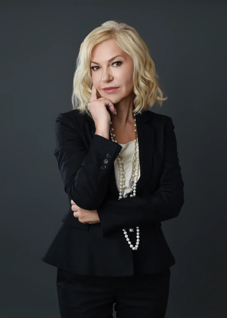 Confident woman with blonde hair wearing a black business suit, thoughtfully posing for a professional glamour photography session