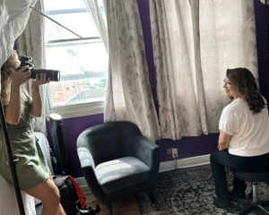 Woman counselor sitting on a stool in front of a backdrop during a professional headshot session