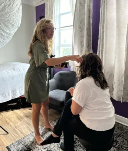 Photographer adjusting a woman's hair during a headshot session in a naturally lit studio.