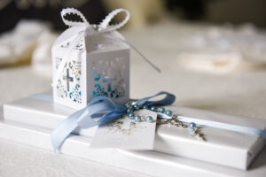 Baptism gift box with a cross design, wrapped in blue ribbon, and a rosary on top of it.