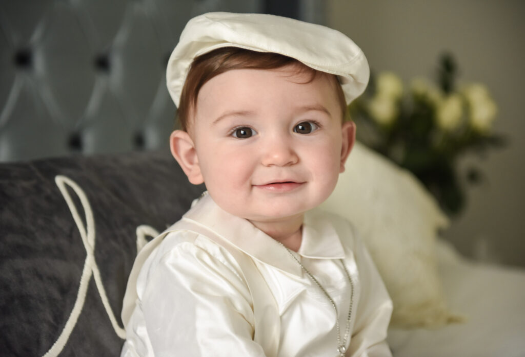 Baptisim baby boy in a white outfit, smiling at the camera.