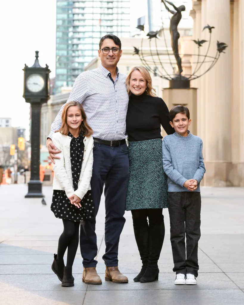 Family of four standing on a city street with modern architecture in the background.